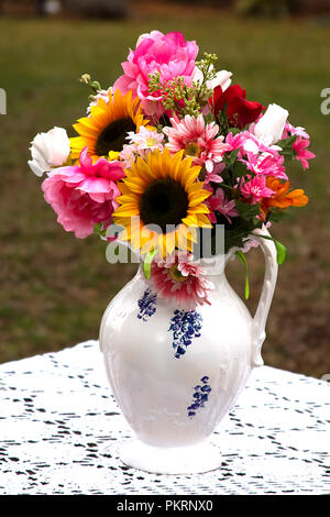 Brocca Vintage vaso riempito con assortimento di fiori sulla tovaglia di pizzo Foto Stock