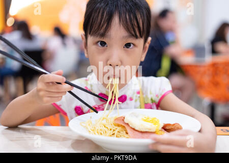 Cinese asiatici bambina mangiare tagliatelle con bacchette in ristorante Foto Stock