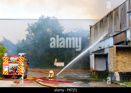 I vigili del fuoco di funzionamento flessibile di acqua diretta a finestre aperte di fabbrica sul fuoco con fumo drifting attraverso la parte superiore del telaio. La fabbrica di Cummins fire a Westwood, Margate. Foto Stock