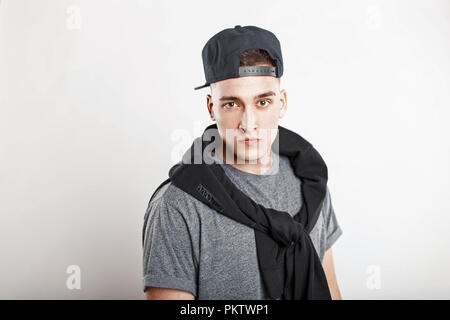 Bel giovane ragazzo in un berretto da baseball con una camicia grigia su sfondo bianco Foto Stock