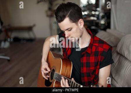 Giovane uomo bello con la chitarra seduta sul lettino Foto Stock