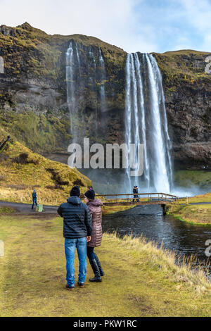 Seljalandsfoss, Islanda - 22 ott 2017 - Coppia giovane godendo il Seljalandsfoss rientrano in un Nuvoloso Giorno in Islanda. Foto Stock