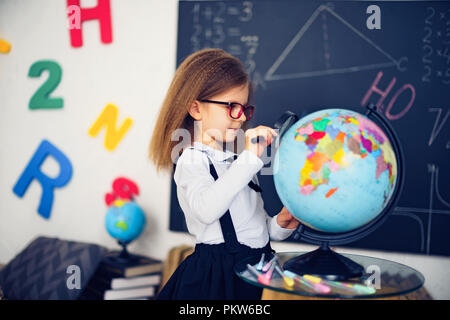 Ritratto di una giovane e bella ragazza schoolgirl esplorando il mondo attraverso una lente di ingrandimento. Giorno della conoscenza. inizio anno scolastico. Studiare la geografia con globo Foto Stock