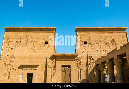 Pilone esterno muri intagliati con figure egiziane e geroglifici e il Tempio di Philae, Agilkia Isola, Fiume Nilo, Aswan, Egitto, Africa Foto Stock