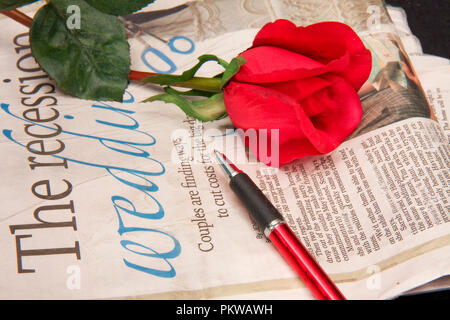 Close-up del giornale con una rosa rossa e la penna appoggiata sulla sommità di esso Foto Stock