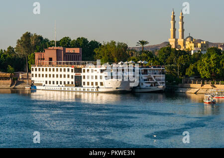 Ormeggiate le grandi navi da crociera sul Fiume Nilo con grande moschea minareti della Moschea El-Tabia, Aswan, Egitto, Africa Foto Stock