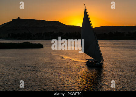 Silhouette di una Felucca tradizionale barca a vela al tramonto, Fiume Nilo, Aswan, Egitto, Africa con collina monumento Qubbet el Hawa Foto Stock