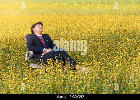 Imprenditore asiatico è sdraiato su una sedia in un grande giallo di campo dei fiori Foto Stock