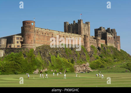 Il castello di Bamburgh, ex casa del re di Northumbria, villaggio partita di cricket Foto Stock