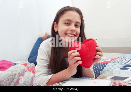 La ragazza si siede nel letto con con un cuore di peluche Foto Stock