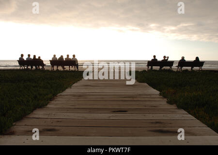 La gente seduta sulle panchine sul lungomare di Playa de Las Americas e guardare il tramonto , Tenerife , Isole Canarie , Spagna . Febbraio 2006 Foto Stock