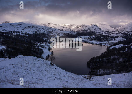 Grasmere presi da Loughrigg Fell, Lake District inglese. Vista serale in inverno con piena copertura di neve e nuvole drammatico. Foto Stock