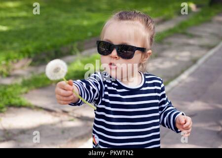 Vista su un piccolo grazioso toddler girl in occhiali da sole nel parco della città su una soleggiata giornata estiva Foto Stock