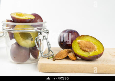 Prugne fresche preparate per inceppamento. Frutti saporiti su una tavola di legno in cucina. Sfondo bianco. Foto Stock