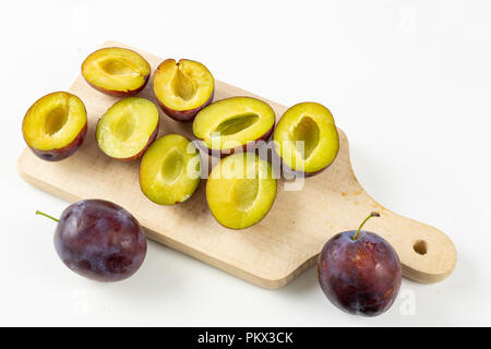 Prugne fresche preparate per inceppamento. Frutti saporiti su una tavola di legno in cucina. Sfondo bianco. Foto Stock