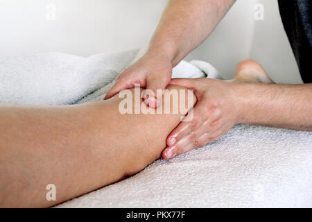 Massaggio delle gambe. Maschio terapista massaggiatore mani facendo applicare pressione impastare sul polpaccio femmina massaggio delle gambe. Massaggiatrice professionale il massaggio piedi della ragazza. Foto Stock