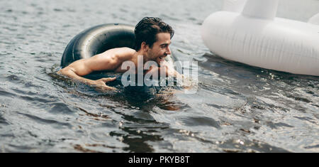 Uomo che utilizza un gonfiabile tubo di gomma a nuotare in un lago. L'uomo godendo la sua vacanza nuotare nel lago utilizzando un salvagente. Foto Stock