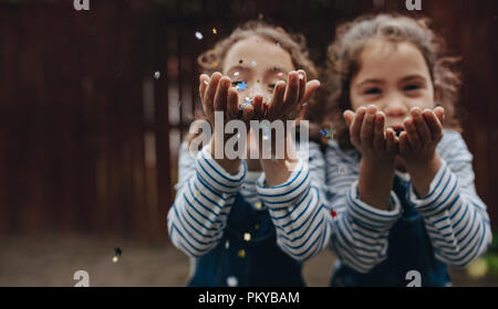 Le giovani ragazze soffiando glitter coriandoli. Gemelle divertendosi e soffiando glitter coriandoli all'esterno. Foto Stock