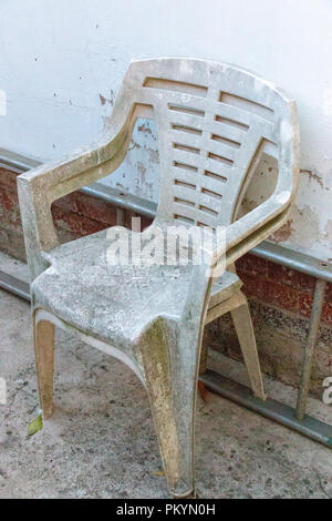 Una vista ravvicinata di due molto vecchie sedie in plastica bianca contro il lato di una scala di metallo e il muro bianco Foto Stock
