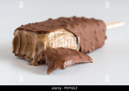 Gelato al cioccolato sul bastone con il fuoco selettivo su morso parte anteriore isolato bianco su sfondo grigio Foto Stock