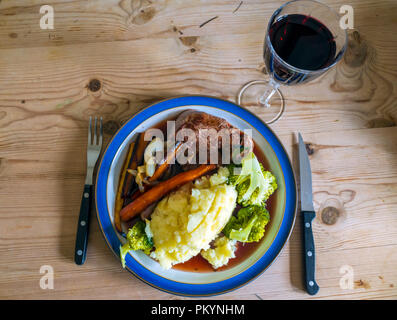 Inglese per la cena di filetto di manzo bistecca con broccoli purè di patate carote arrosto Pastinaca Radici di cipolle e sugo di carne e un bicchiere di vino rosso Foto Stock