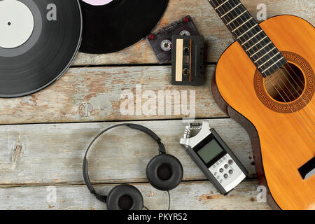 Vintage attrezzature musicali su tavole di legno. Dischi in vinile, cassette a nastro, chitarra acustica, registratore vocale e cuffie moderne. Evoluzione di technolog Foto Stock