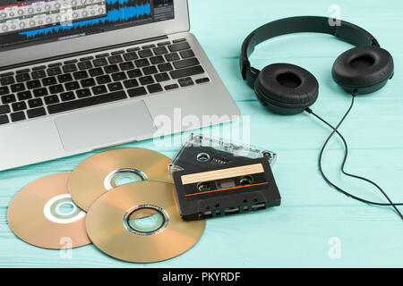 Antiche e Moderne attrezzature su sfondo di legno. Laptop, cuffie audio cassette a nastro e compact disc sul blu sullo sfondo di legno. Spazio di lavoro di dj. Foto Stock