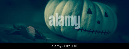 Decorate a mano con zucca faccia dipinta e foglie di autunno sul tavolo di legno . Dark, moody e spooky Halloween banner. Foto Stock