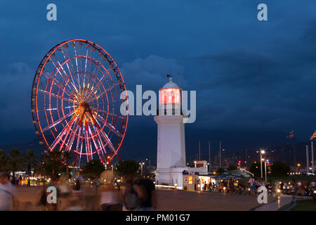 Vista notturna sulla illuminata ruota panoramica Ferris e il faro a Batumi, Georgia Foto Stock
