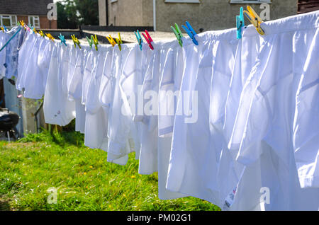 Camicie bianche appendere fuori ad asciugare su una linea di lavaggio in una zona residenziale giardino sul retro. Foto Stock