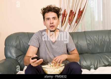 Uomo con birra e popcorn guardando la TV a casa Foto Stock