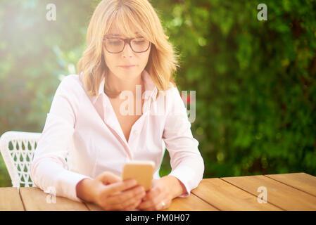 Alta angolazione della donna di mezza età seduta al di fuori mentre usando il suo cellulare e per la messaggistica di testo. Foto Stock