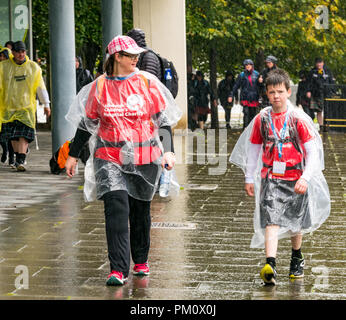 Leith, Edimburgo, Scozia, Regno Unito, 16 settembre 2018. Edinburgh Kilt Walk, sponsorizzato dalla Royal Bank of Scotland, si svolge oggi. I camminatori raccogliere fondi per un'associazione benefica di loro scelta. I kilt camminatori raggiungono il miglio 14 sotto la pioggia. Una donna e un ragazzo camminano lungo la riva del fiume indossando ponchi di pioggia che sollevano i soldi per la carità dell'ospedale dei bambini di Edinburgo. Il ragazzo indossa un kilt. Foto Stock