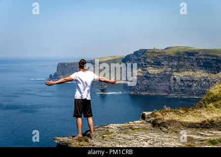 L'uomo gode della vista sull'oceano dalle scogliere di Moher, scogliere sul mare situate al margine sud-occidentale della regione di Burren nella contea di Clare, Irlanda Foto Stock