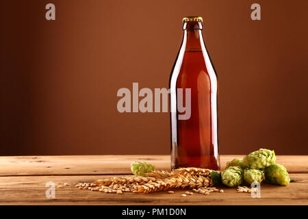 Chiudere uno pieno unopen senza etichetta flacone in vetro marrone di birra, verde luppolo, orzo e grano spike sul tavolo di legno, basso angolo vista laterale Foto Stock