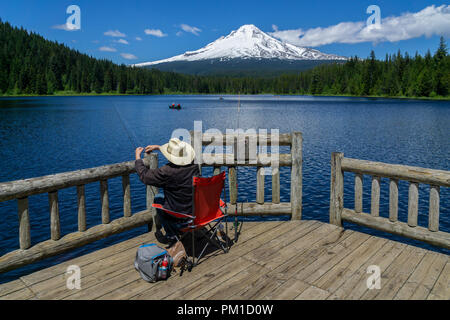 Pescatore all'Trillium Lago con il cofano Mt ricoperta di neve in background su una bella giornata soleggiata di tarda primavera, Oregon, Stati Uniti d'America. Foto Stock