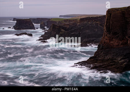 Il selvaggio Oceano Atlantico si blocca contro il mare di pile, rocce e scogliere lungo la costa occidentale delle Isole Shetland a Eshaness Foto Stock