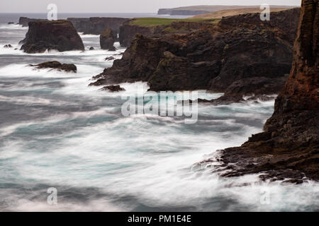 Il selvaggio Oceano Atlantico si blocca contro il mare di pile, rocce e scogliere lungo la costa occidentale delle Isole Shetland a Eshaness Foto Stock