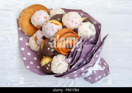 Bouquet realizzati da diversi gustosi panini e ciambelle giace su un bianco tavolo in legno Foto Stock