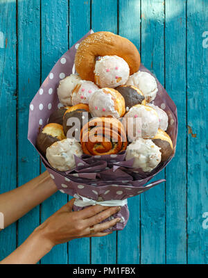 Ragazza con un bouquet costituito da diversi gustosi panini e ciambelle su un blu sullo sfondo di legno Foto Stock