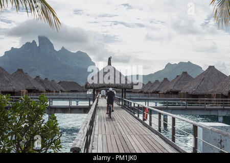 Uomo bicicletta equitazione all'isola di Bora Bora con il Monte Otemanu dietro, Polinesia Francese Foto Stock