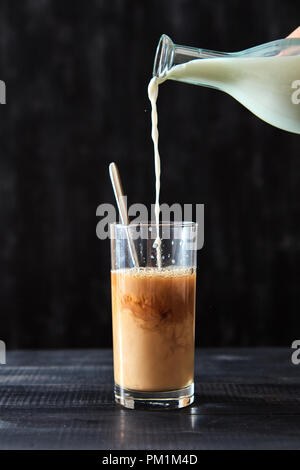 In preparate di fresco caffè in un vetro trasparente versare il latte in un tavoli in legno nero. Deliziosi drink di mattina. Foto Stock