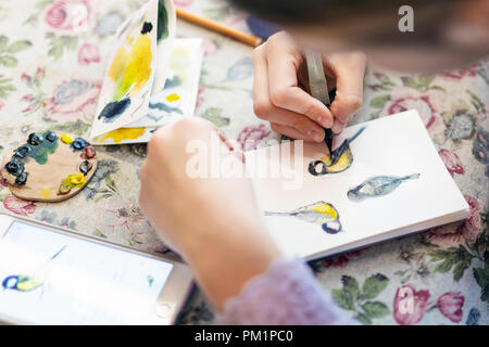 Ragazza adolescente disegno di uccelli nel piccolo disegno carta-pad. Close-up kid artista pittura foto piccola sul blocco di carta con la spazzola. I bambini la creatività con Foto Stock