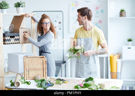 Due giovani fioristi di parlare nel loro studio durante la preparazione di pacchetto e rendendo mazzi floreali Foto Stock