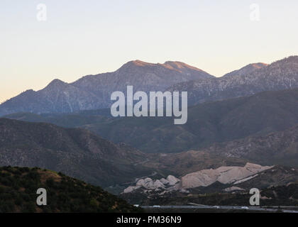 Bello sfondo sullo sfondo di un paesaggio di montagna con una strada piena di automobili e camion al fondo. Foto Stock