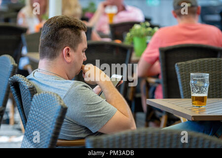 RIGA, Lettonia - 31 luglio 2018: un uomo è seduto in un bar, bere birra e la lettura di un messaggio di testo sul telefono. Foto Stock