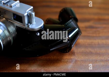 Una parte di una vecchia foto fotocamera con uno stile rétro bobina (bobina) film 35 mm avvolto su sfondo di legno. Parte frontale superiore vista laterale Foto Stock