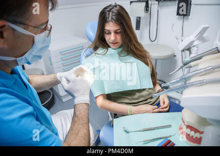 Medico professionale il processo di dimostrazione di denti sani la spazzolatura di giovane donna seduto in poltrona. Foto Stock