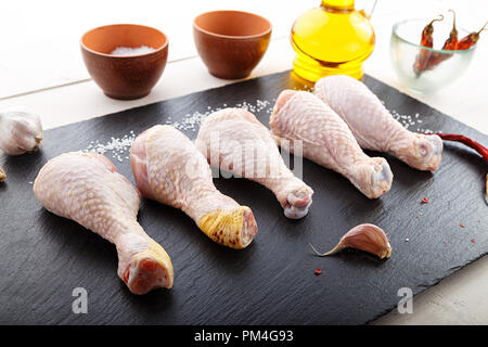Materie le cosce di pollo rivestito in una riga sulla lavagna, vi sono un certo numero di spezie - sale, pepe, olio d'oliva e aglio Foto Stock