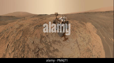 Questo autoritratto della NASA Curiosità Mars rover mostra il veicolo presso il 'Mojave' sito, dove praticare il suo raccolto la missione secondo il gusto del monte Sharp. La scena unisce decine di immagini prese durante il mese di gennaio 2015 dal Marte lente mano Imager (MACLI) fotocamera alla fine del rover del braccio robotico. Il pallido 'Pahrump Hills' affioramento circonda il rover, e la porzione superiore del monte Sharp è visibile all'orizzonte. La massa scura in alto a destra e in basso a sinistra contiene increspature di vento-soffiato di sabbia e polvere. Riferimento al file # 1003 575THA Foto Stock